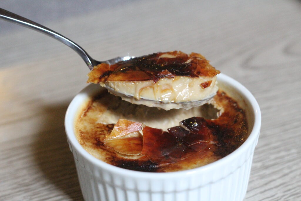 A spoonful of creme brulee above the ramekin of creme brulee