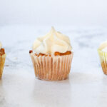four sweet potato fluff cupcakes lined up horizontally across the image, on a white marbled surface, with a greyish white background