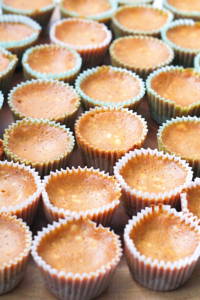 close up, angled view of the tops of a bunch of pumpkin pie cheesecakes in paper liners