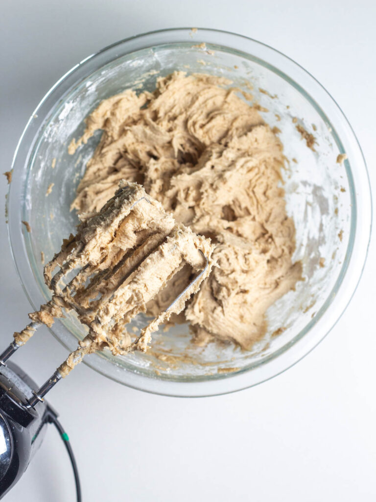 Beaters over a mixing bowl of cinnamon brown sugar buttercream frosting.
