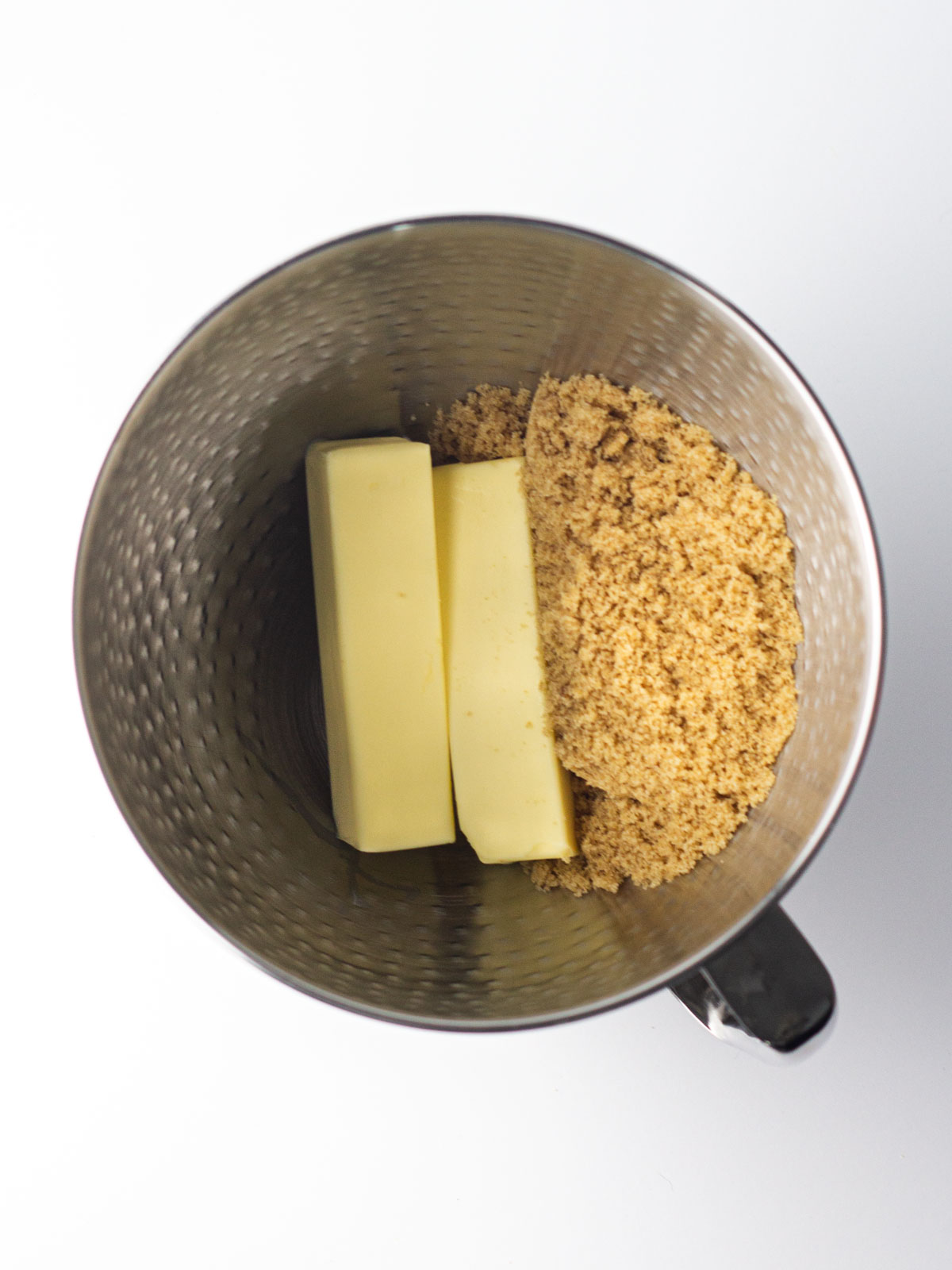 Two sticks of butter and brown sugar in a silver mixing bowl.