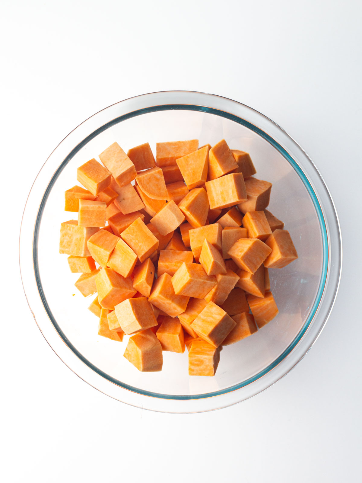 Cubed sweet potatoes in a clear glass mixing bowl.