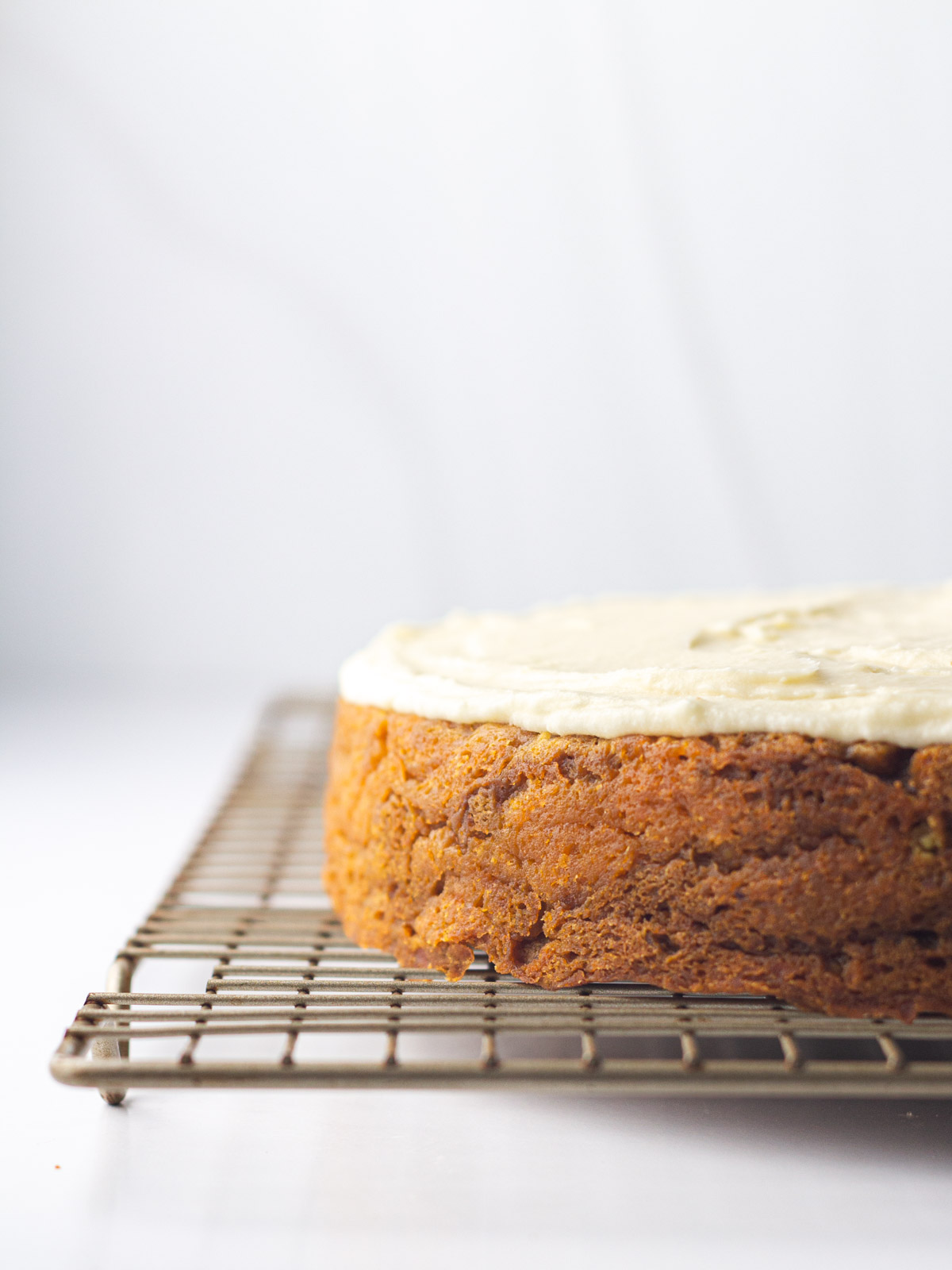 A frosted sweet potato cake on a gold wire rack going out of frame on the right.