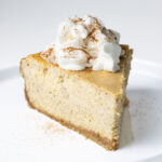 A slice of pumpkin pie cheesecake topped with a dollop of whipped cream and a sprinkle of cinnamon.