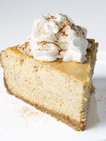 A slice of pumpkin pie cheesecake topped with a dollop of whipped cream and a sprinkle of cinnamon.