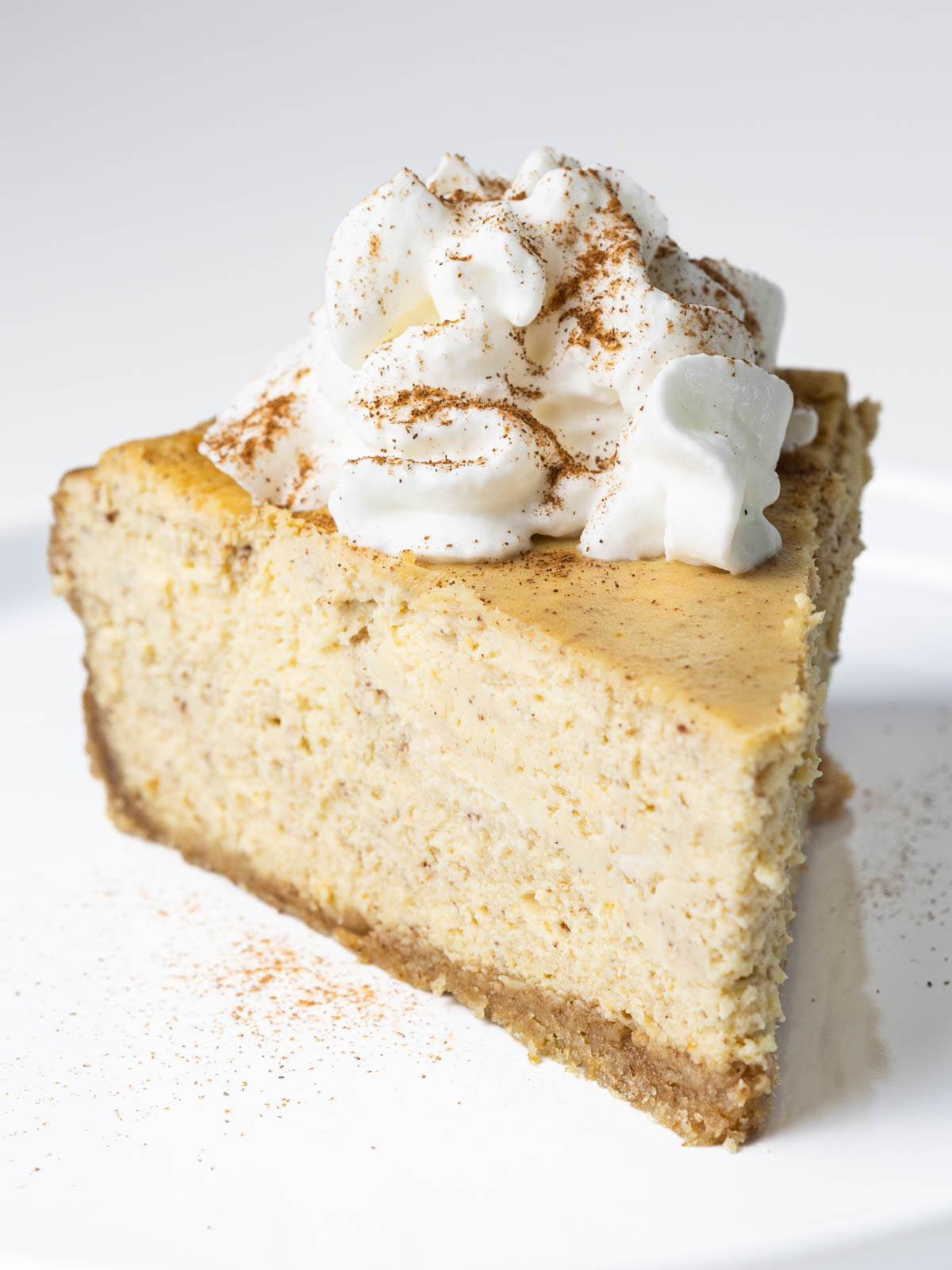A slice of pumpkin pie cheesecake topped with a dollop of whipped cream and a sprinkle of cinnamon.