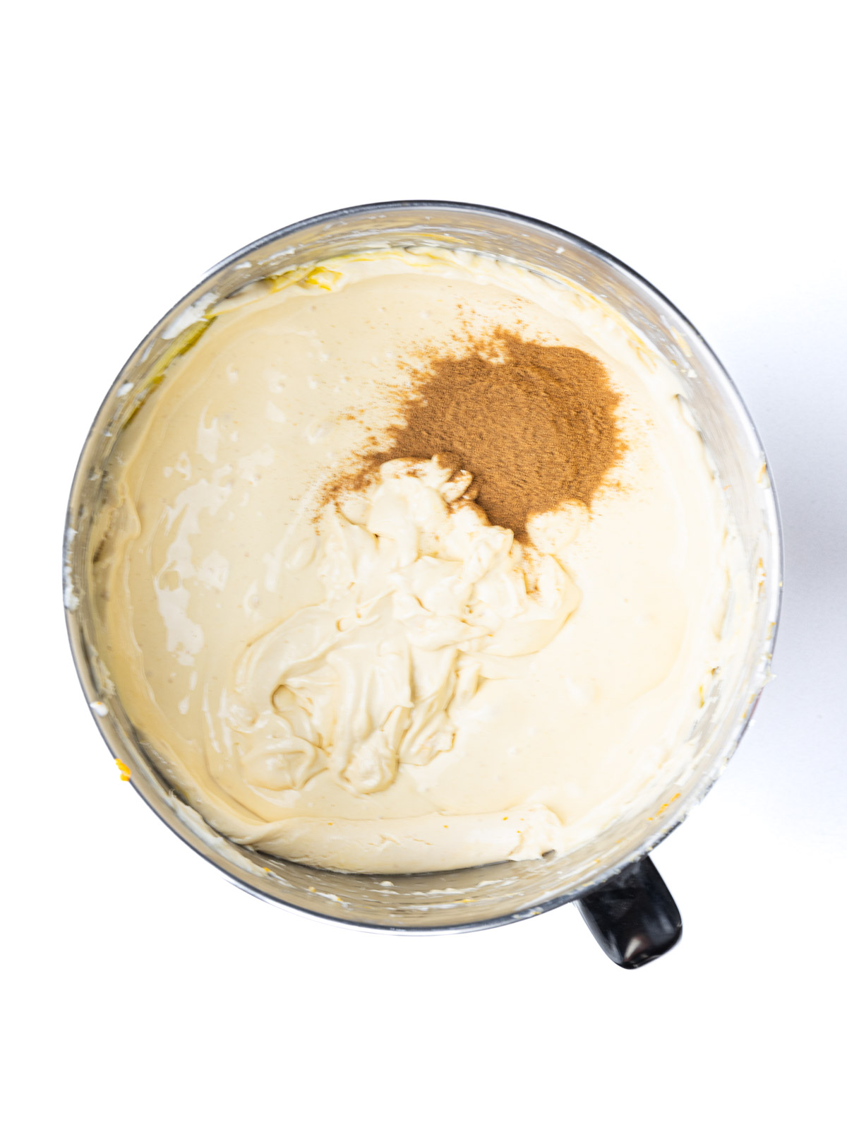 Pumpkin pie spice added to the pumpkin cheesecake mixture in a mixing bowl.