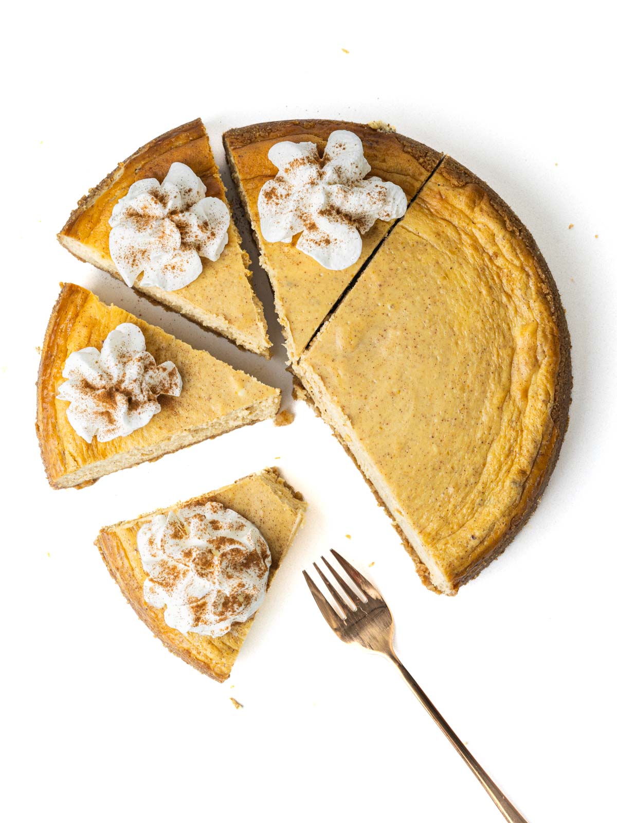 A partially sliced pumpkin pie cheesecake with whipped cream on the slices and a fork next to a partially eaten slice.