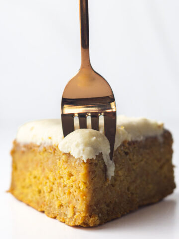 A hand sticking a rose gold fork into a slice of frosted sweet potato cake.