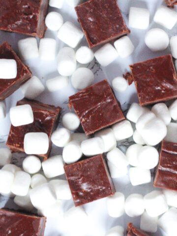 Top down view of a bunch of cubes of brown hot cocoa fudge surrounded by a bunch of mini marshmallows