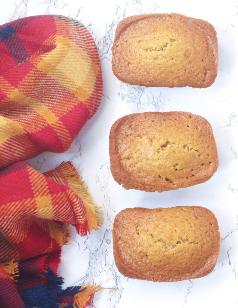 top down view of three chai loaves each laying horizontally forming a vertical row on a white marble surface next to a red and gold plaid scarf or blanket