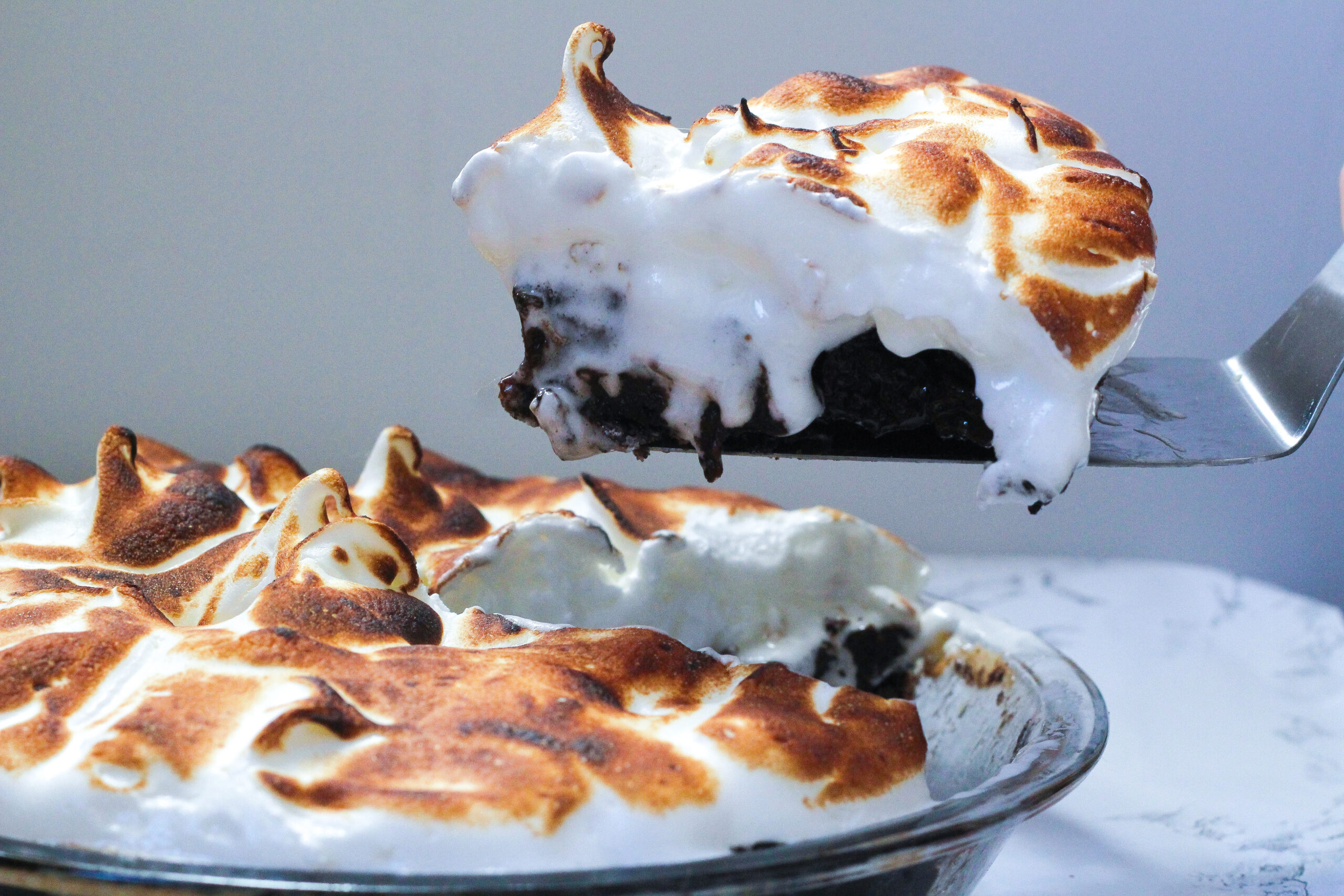 Side view of a mocha meringue pie on the left, with a single slice being lifted out on a pie server on the right
