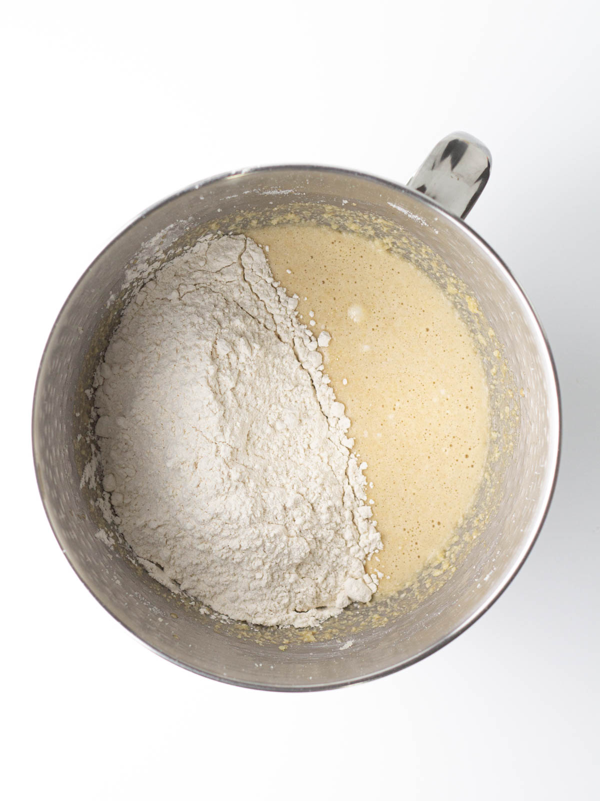 Flour sitting on top of chai bread batter in a silver mixing bowl.