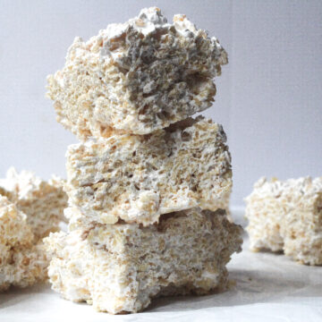 A stack of 3 maple rice krispie treats on a white marbled surface in front of a grey background and a few more maple rice krispie treats in a single layer