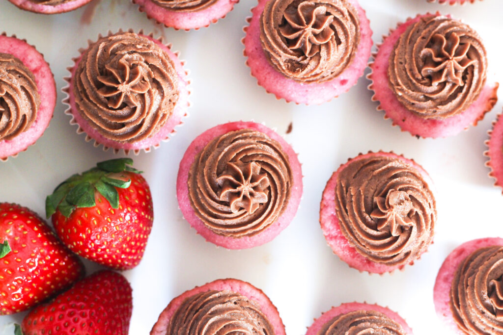 mini strawberries and champagne cupcakes with chocolate buttercream frosting next to three strawberries.