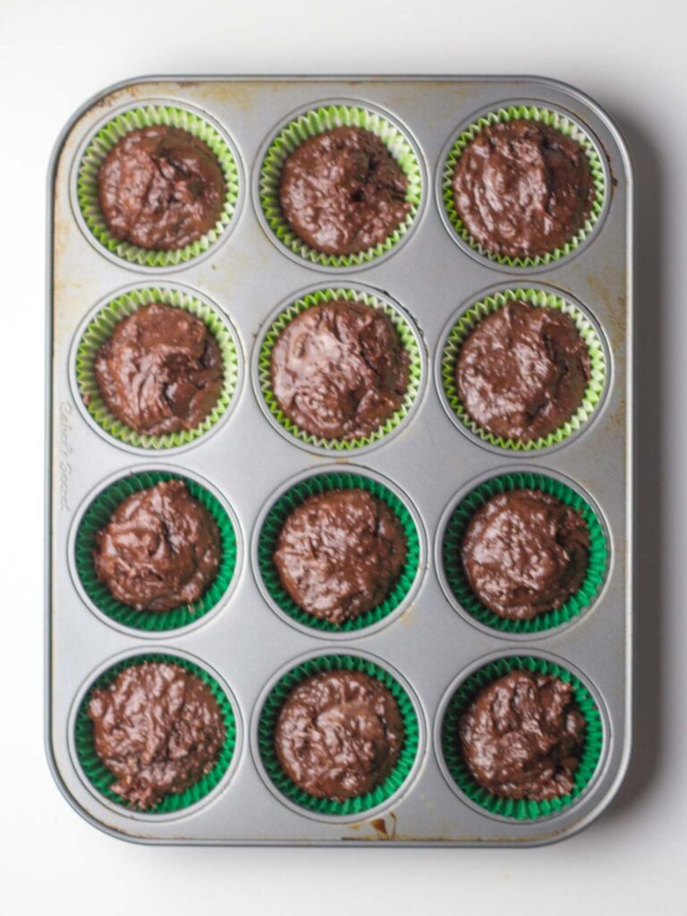 Un-baked cupcake batter in green liners in a 12 cup cupcake pan.