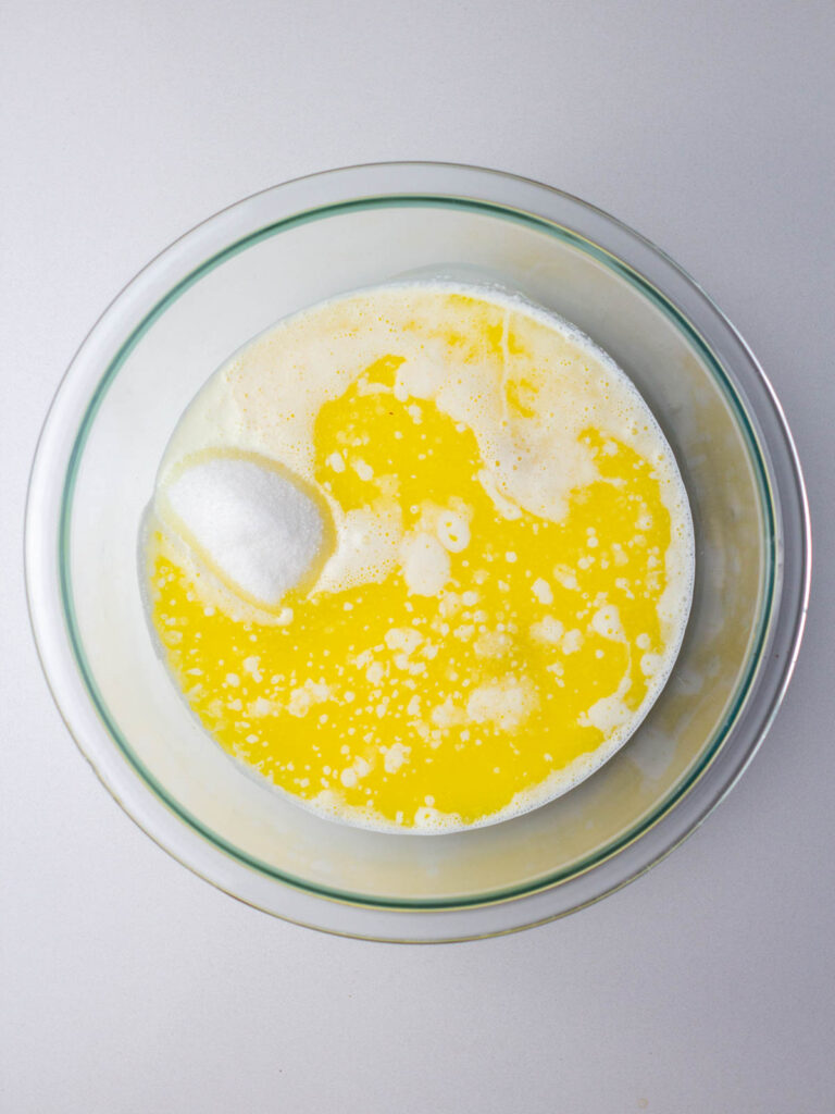 Cream, sugar, eggs, and melted butter in a clear glass mixing bowl.