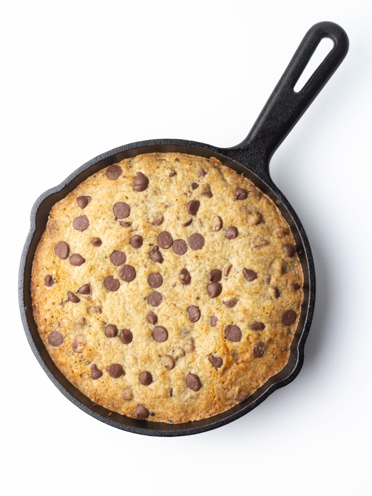 A baked chocolate chip cookie in a cast iron skillet.
