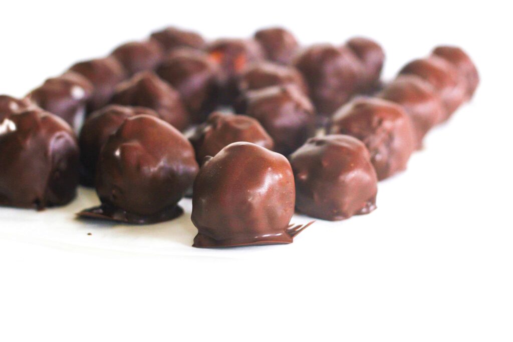 Batch of chocolate covered mint julep bourbon balls on white surface.