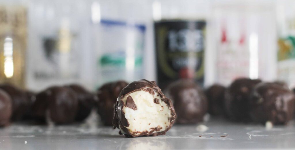 Bite of chocolate covered mint julep bourbon ball with Kentucky Derby glasses in the background.