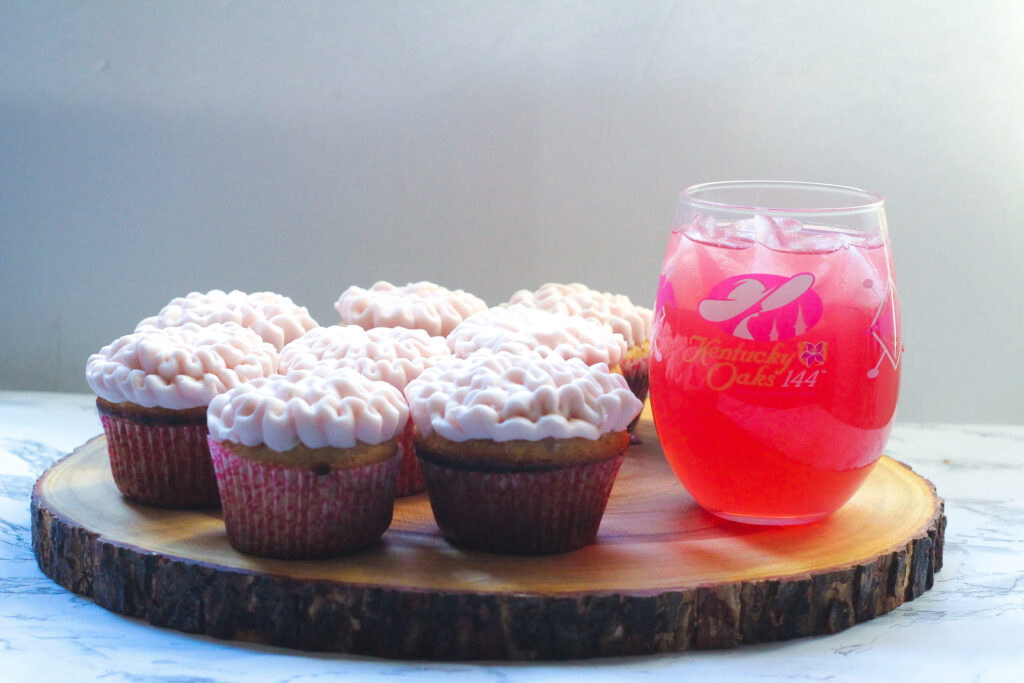 Kentucky Oaks Lily Cupcakes with pink frosting with an Oaks Lily cocktail in a stemless glass.