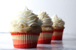three bourbon peach sweet tea cupcakes in a diagonal line in red, white, and pink wrappers on a marbled surface in front of a white background