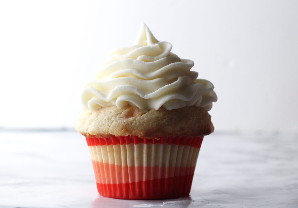 a bourbon peach sweet tea cupcake topped with frosting in a pink ombre paper cupcake liner.