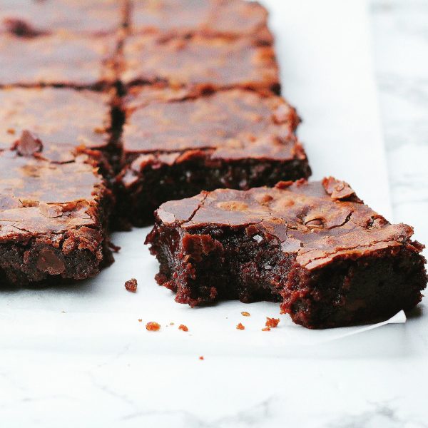 885AC37B-9102-4034-9B2F-8628F0A7447F Close up batch of fudgy brownies on parchment paper on top of a marble surface with the front right brownie pulled out at an angle with a bite taken out of it and some crumbs in front of the bite mark