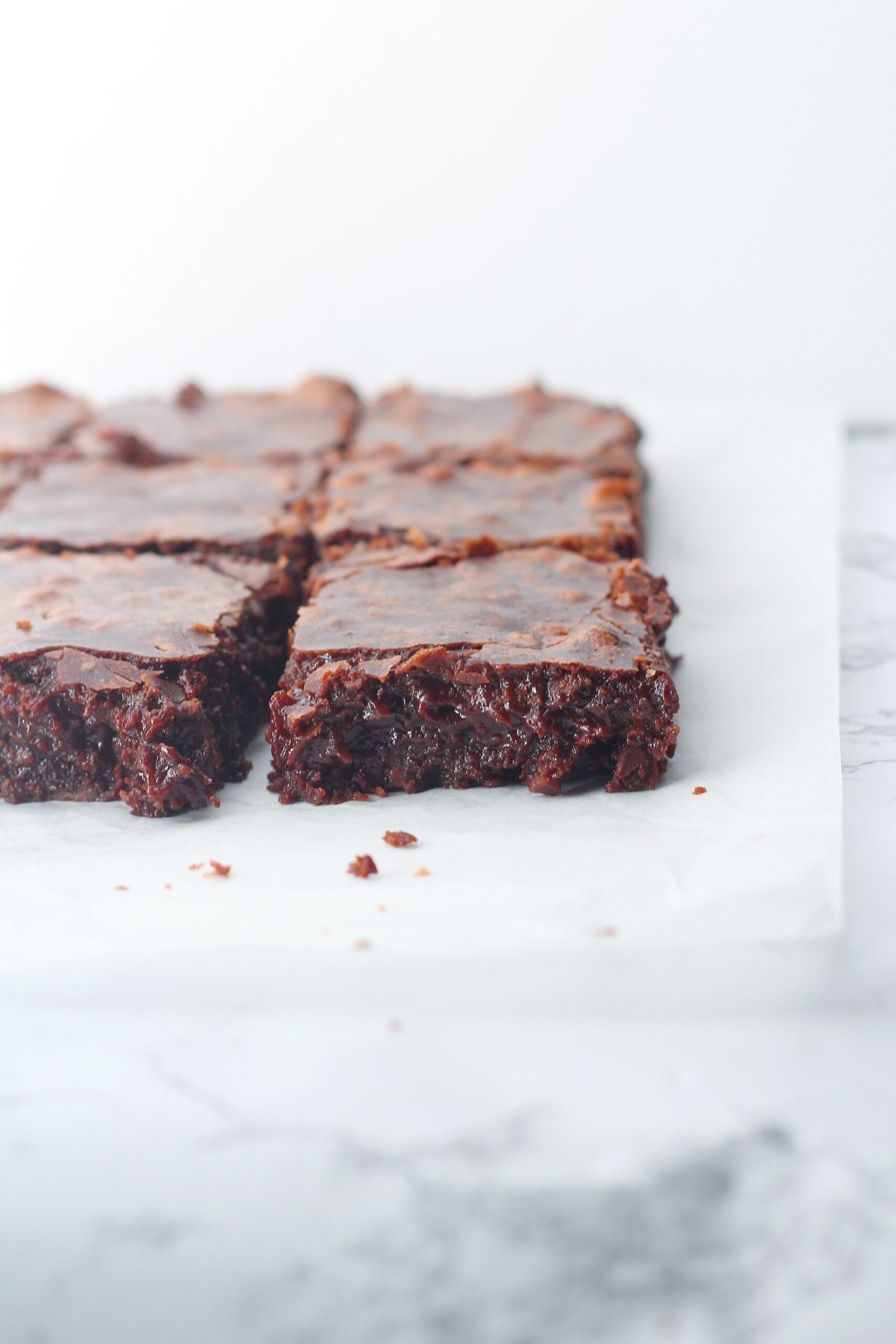 Fudgy brownies on a piece of parchment paper on top of a marble surface