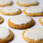 Angled view of beer cookies topped with a white icing glaze on a white surface.