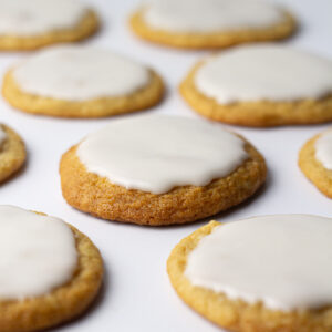 Angled view of beer cookies topped with a white icing glaze on a white surface.