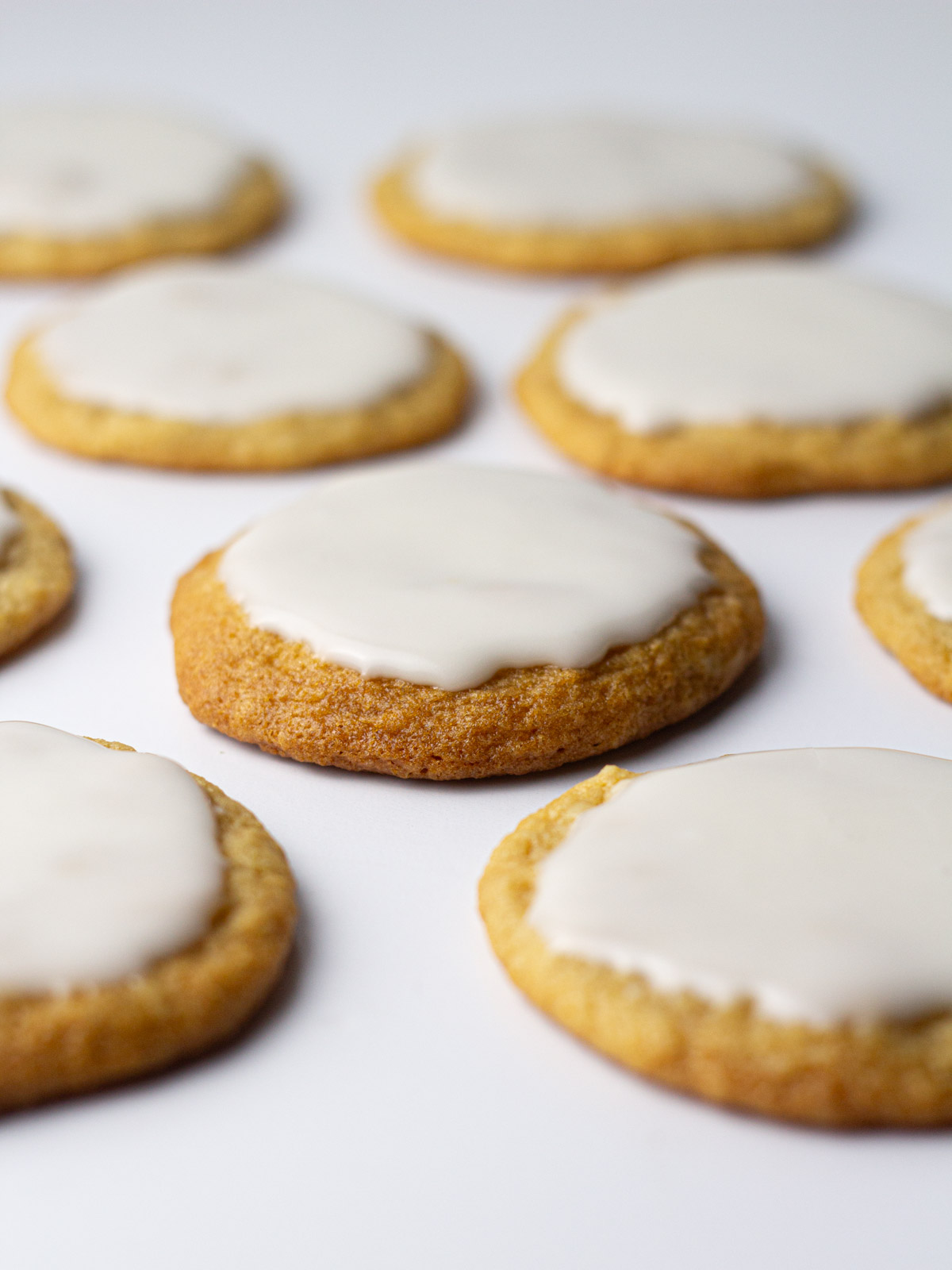 Angled view of beer cookies topped with a white icing glaze on a white surface.