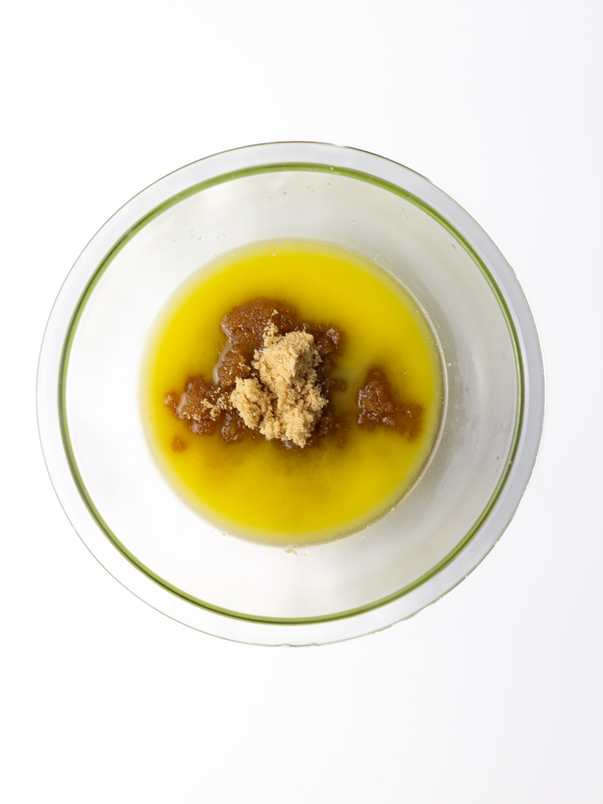 Melted butter and brown sugar in a glass mixing bowl on a white surface.