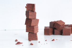 Stack of 5 pieces of smoky bourbon chocolate fudge with the top piece with a bite taken out of it. In the back right of the frame is a pile of fudge.