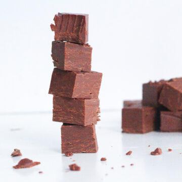 Stack of 5 pieces of smoky bourbon chocolate fudge with the top piece with a bite taken out of it. In the back right of the frame is a pile of fudge.