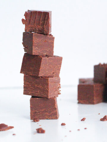 Stack of 5 pieces of smoky bourbon chocolate fudge with the top piece with a bite taken out of it. In the back right of the frame is a pile of fudge.