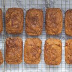 top down view of two horizontal rows of mini pumpkin chai breads, with each mini loaf laying vertically. The loaves are on a wire rack, and the bottom left roll is slightly tilted out of line
