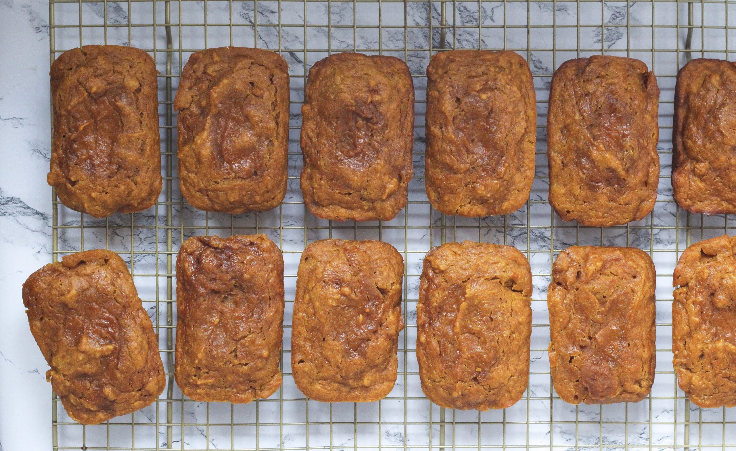 top down view of two horizontal rows of mini pumpkin chai breads, with each mini loaf laying vertically. The loaves are on a wire rack, and the bottom left roll is slightly tilted out of line