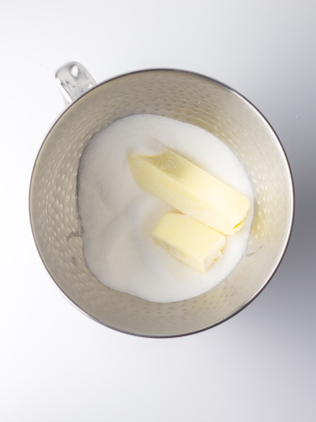 Butter and sugar in a silver mixing bowl.