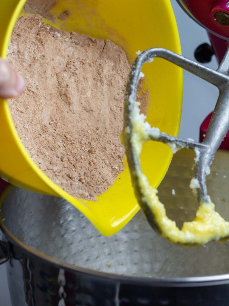 Yellow bowl of dry ingredients bring poured into the mixing bowl on a stand mixer.