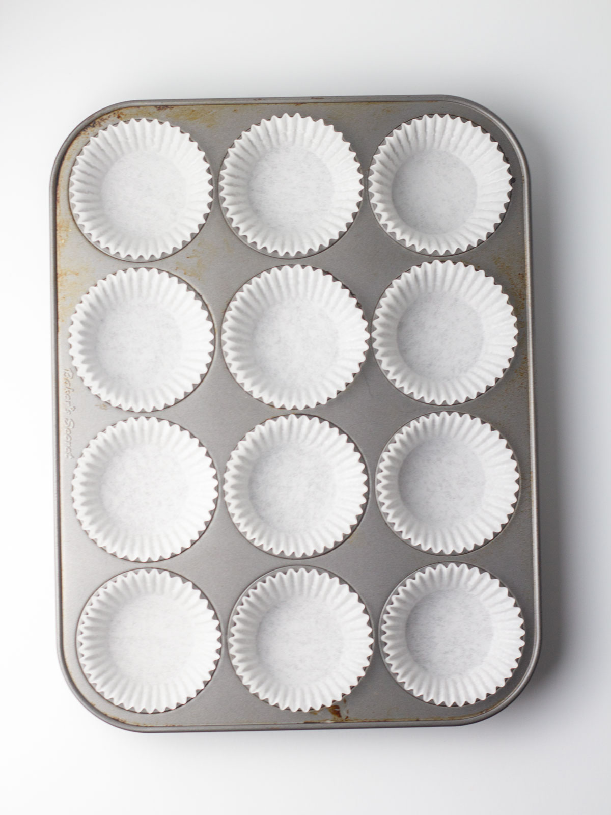 A 12 cup muffin tin lined with white paper liners.