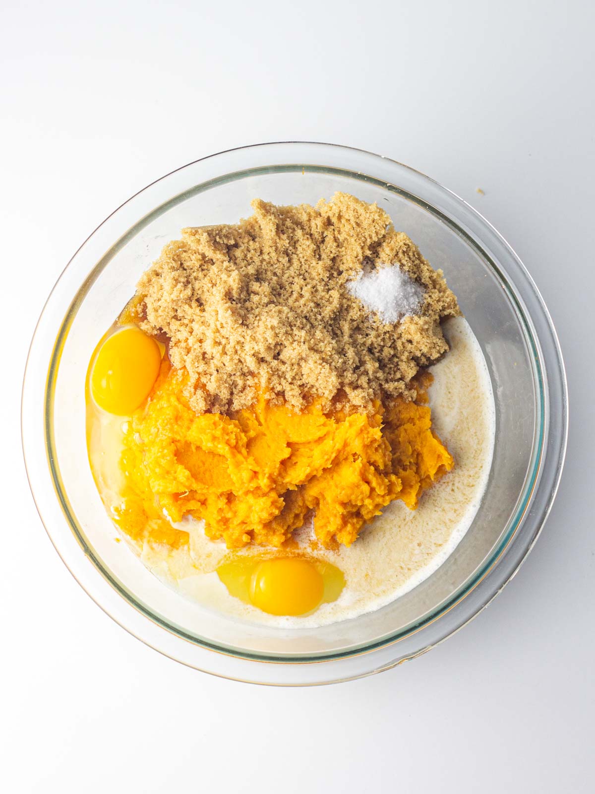 All the sweet potato pie filling ingredients in a clear, glass mixing bowl.