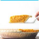Pin for Pinterest of a slice of sweet potato pie being lifted out of the rest of the pie dish which is sitting on a round wooden plank.