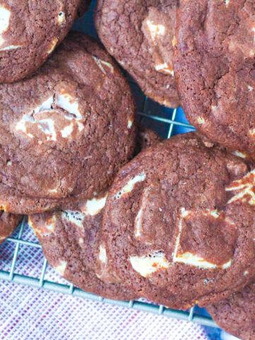 a pile of fudgy peppermint chocolate cookies on a wire rack, angled in the photo. Underneath the front left corner of the wire rack is a red and white napkin also angled across the frame.