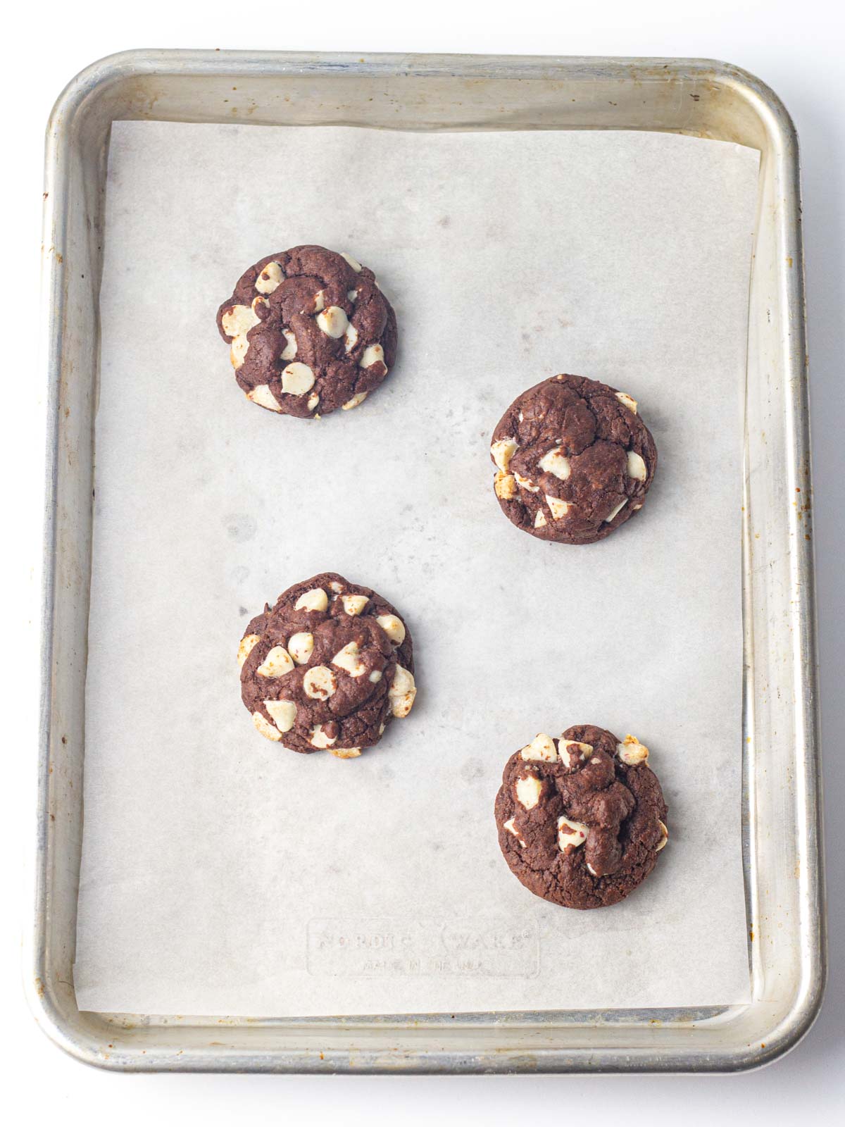 Four baked chocolate peppermint cookies on a parchment lined cookie sheet.