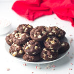A white plate of chocolate peppermint cookies with a red linen in the background and crust peppermint surrounding the scene.