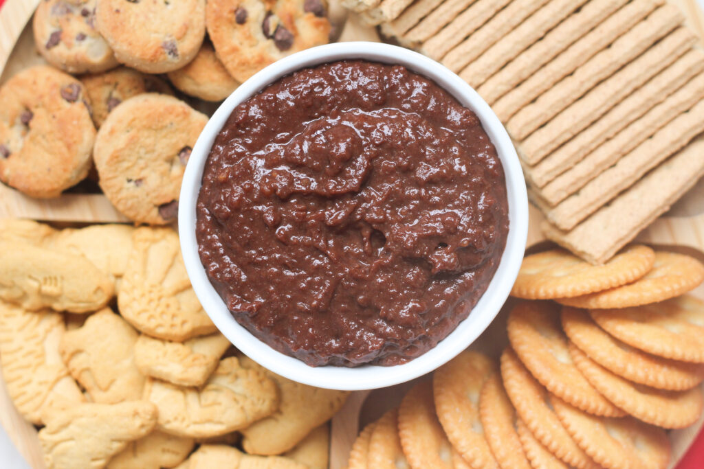 a white bowl of Nutella hummus surrounded by cookies and crackers.