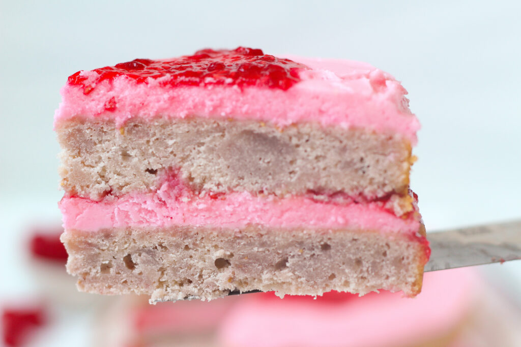 Close up of a slice of rasberry rosè cake layered with pink frosting and red jam.