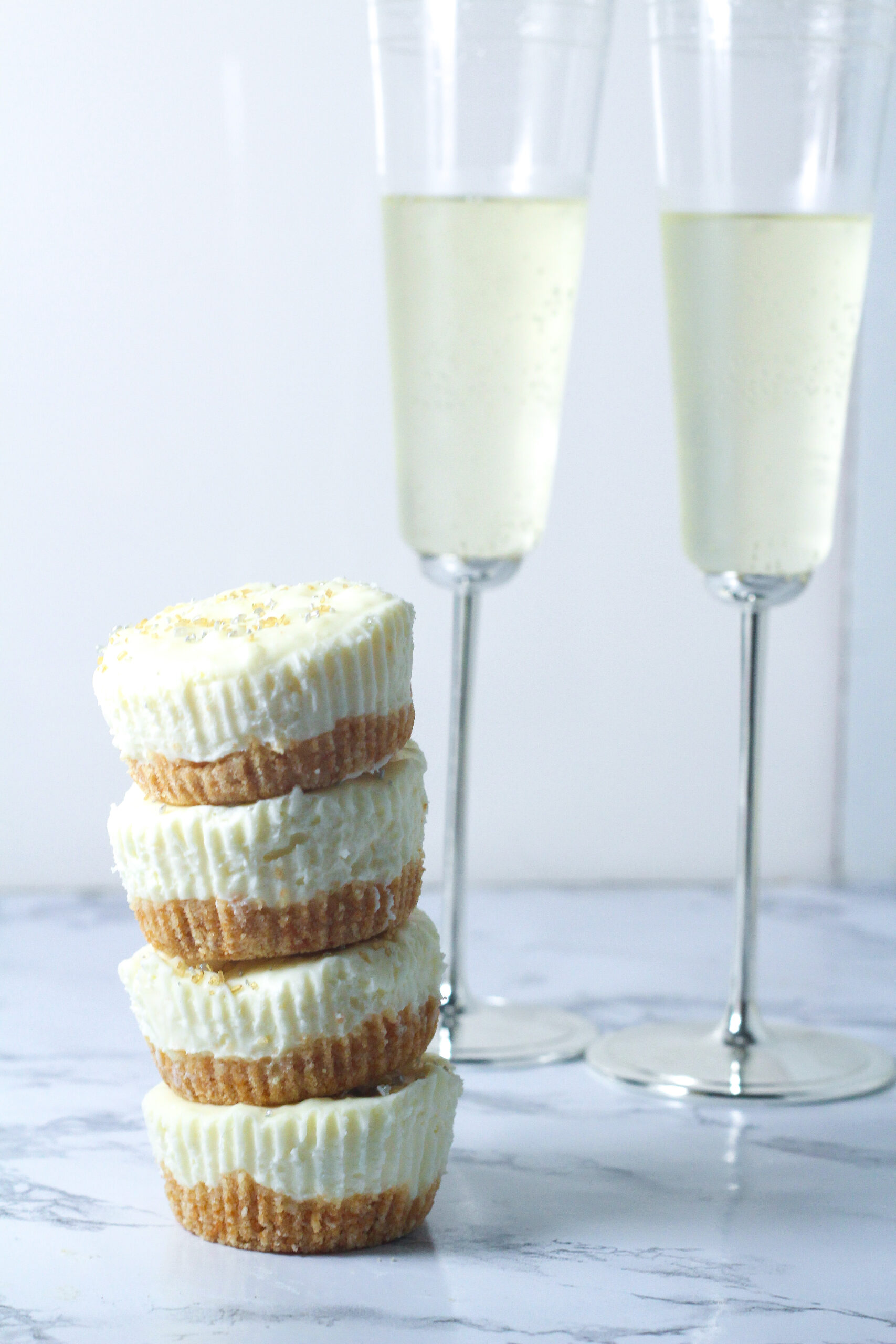 stack of 4 prosecco cheesecakes to the front left of two flutes of champagne on a marbled surface
