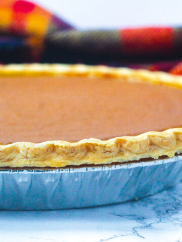 Side view of a bourbon pumpkin pie slightly off to the left of the frame with a red and gold plaid scarf in the background